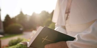 New Report Exposes Decades Of Abuse Person in white robe holding a Bible outdoors