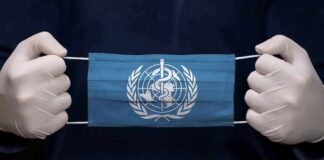 Gloved hands holding a blue face mask with a medical emblem