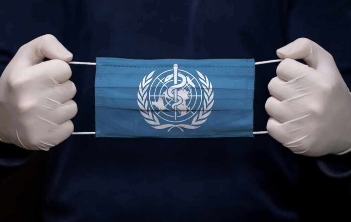 Gloved hands holding a blue face mask with a medical emblem