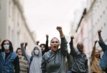 Street War Erupts Over Empty Wallets protester with raised fist leading a crowd in a city street