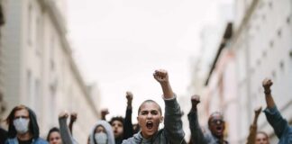 Street War Erupts Over Empty Wallets protester with raised fist leading a crowd in a city street