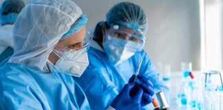 Scientists in protective gear working with a syringe in a laboratory
