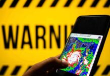 Dangerous Surge Aims Straight At The Carolinas Hand holds smartphone showing cyclone radar map against warning sign