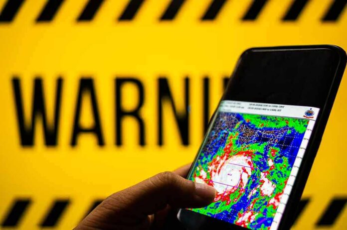shutterstock_1748048666 Hand holds smartphone showing cyclone radar map against warning sign