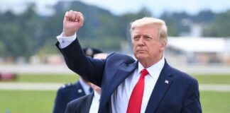 Airport Blast Triggers Trump War Tease man in suit raising a clenched fist outdoors