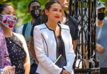 Champagne Stays Cloud AOC’s Class War woman in white blazer holding a tablet at an outdoor gathering