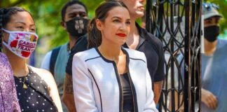 Champagne Stays Cloud AOC’s Class War woman in white blazer holding a tablet at an outdoor gathering