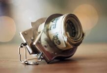 Handcuffs holding a roll of U.S. dollar bills on a table