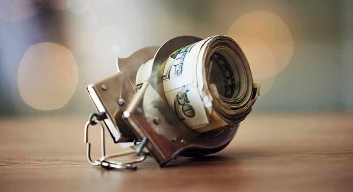 Handcuffs holding a roll of U.S. dollar bills on a table