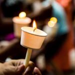 Hand holding a lit candle in a paper drip guard