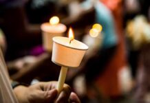 Hand holding a lit candle in a paper drip guard