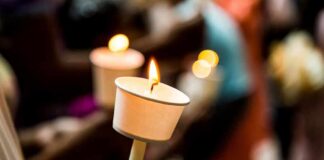 Hand holding a lit candle in a paper drip guard