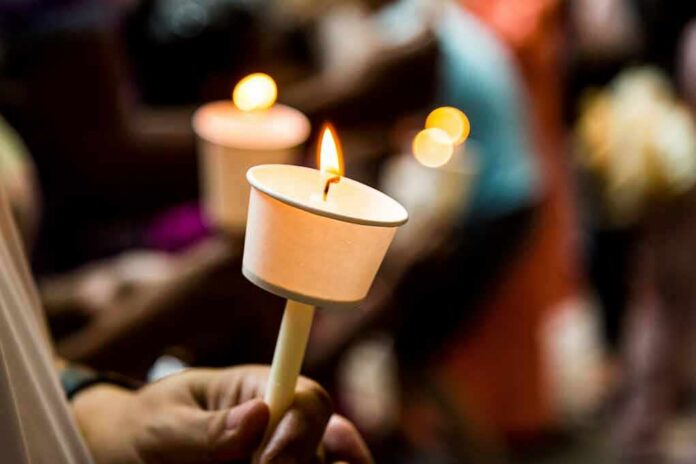 Hand holding a lit candle in a paper drip guard