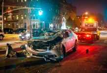 Fiery Red-Light Smash Ends In Murder Wrecked silver car on city street at night with tow truck nearby