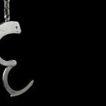 Open metal handcuff hanging against a black background