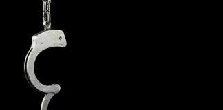 Open metal handcuff hanging against a black background