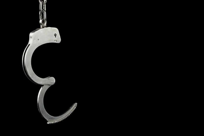 Open metal handcuff hanging against a black background